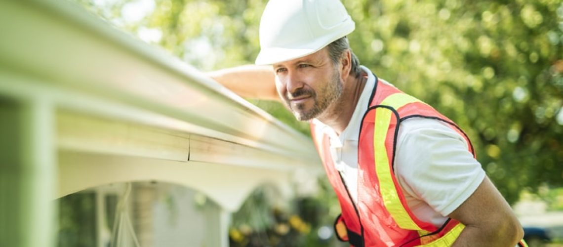 A man with hard hat standing on steps inspecting house roof